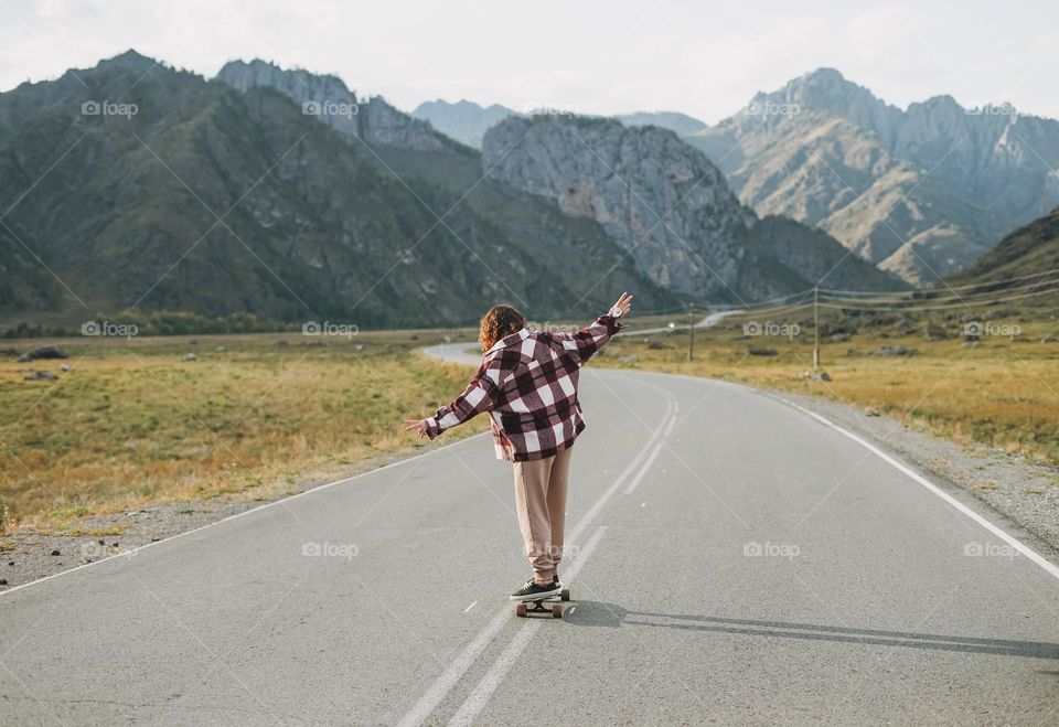 Young woman on skateboard on road against beautiful mountain landscape, Chuysky tract, Altai