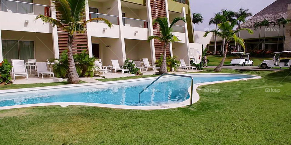 Swimming Pool outside of swanky hotel on a tropical island. Lounge chairs and gold carts and palm trees in view.
