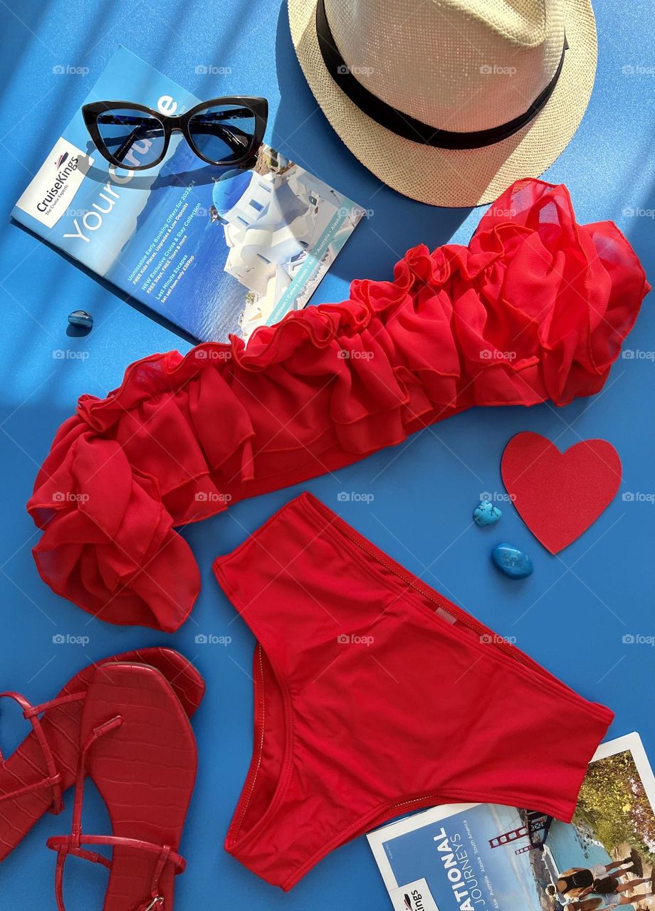 The flatly on vacation theme. Red bikini, sunglasses, hat, sandals and travel magazines.