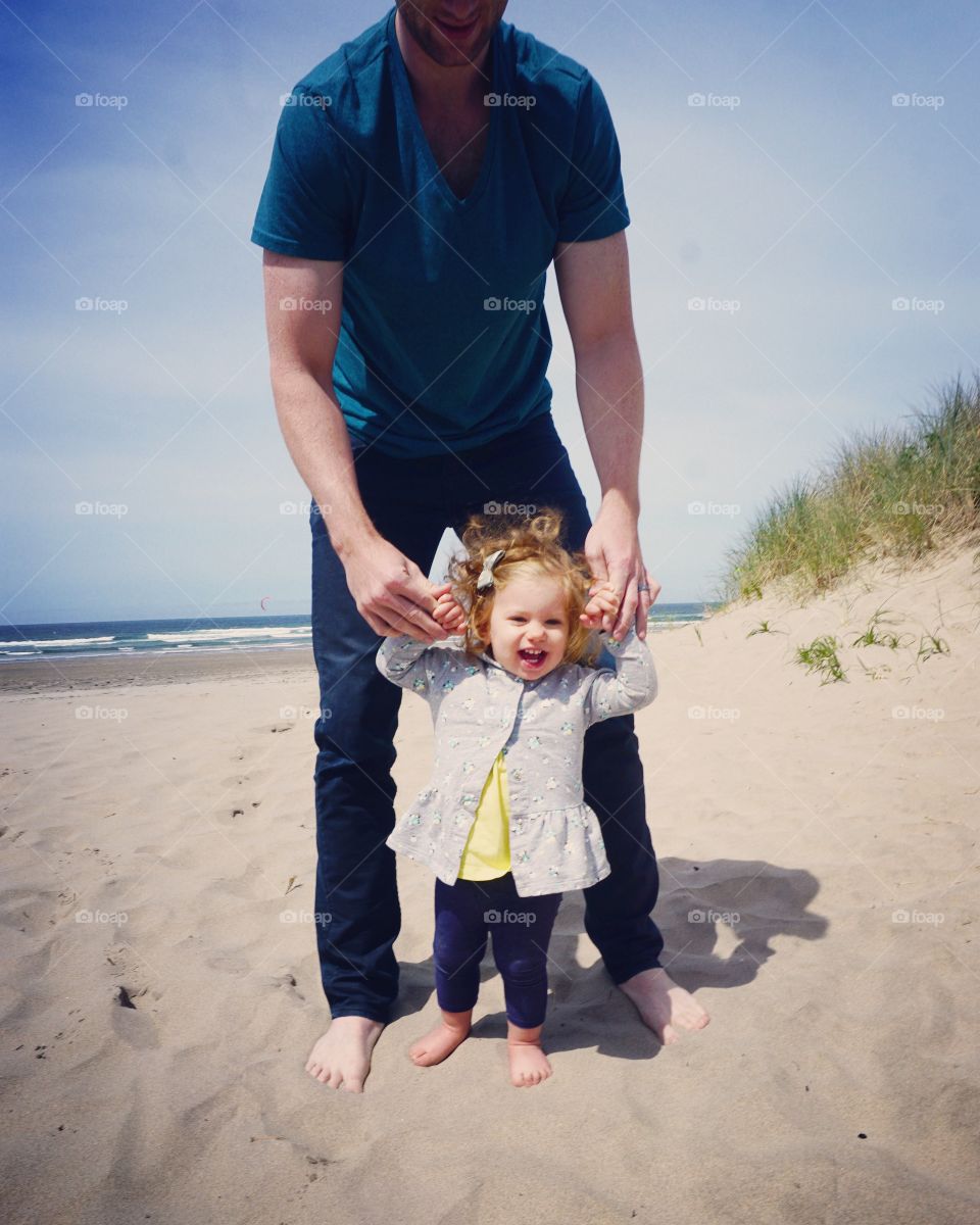 A little toddler girl with father standing at beach
