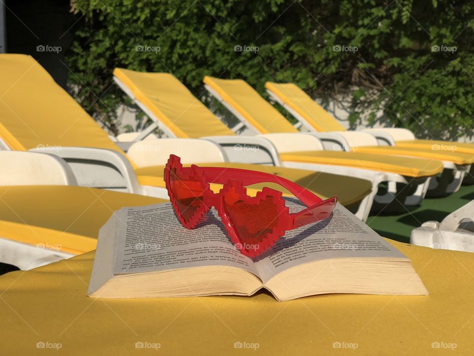 Pink sunglasses and a book placed on a yellow sunbed with many yellow sunbeds in the background