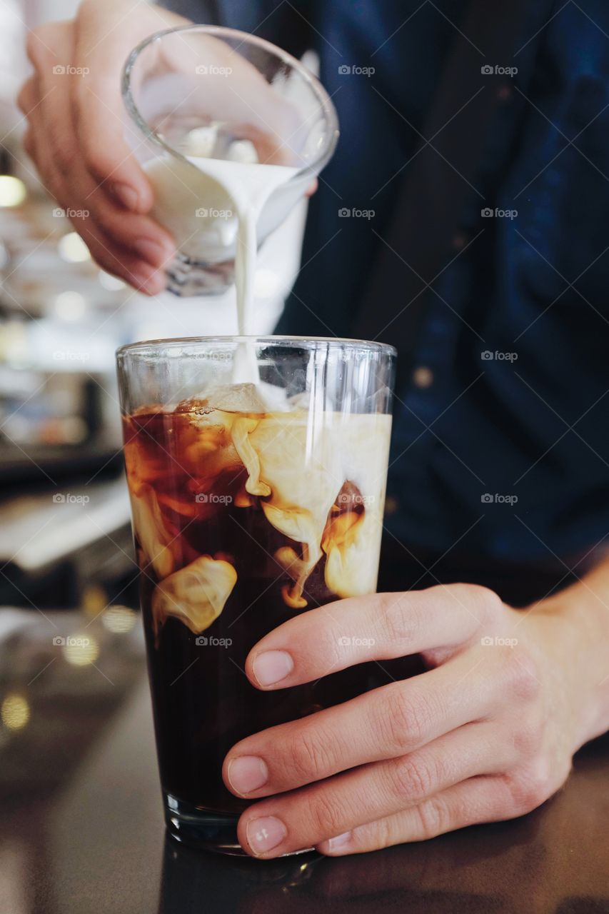 Person's hand pouring milk over iced coffee