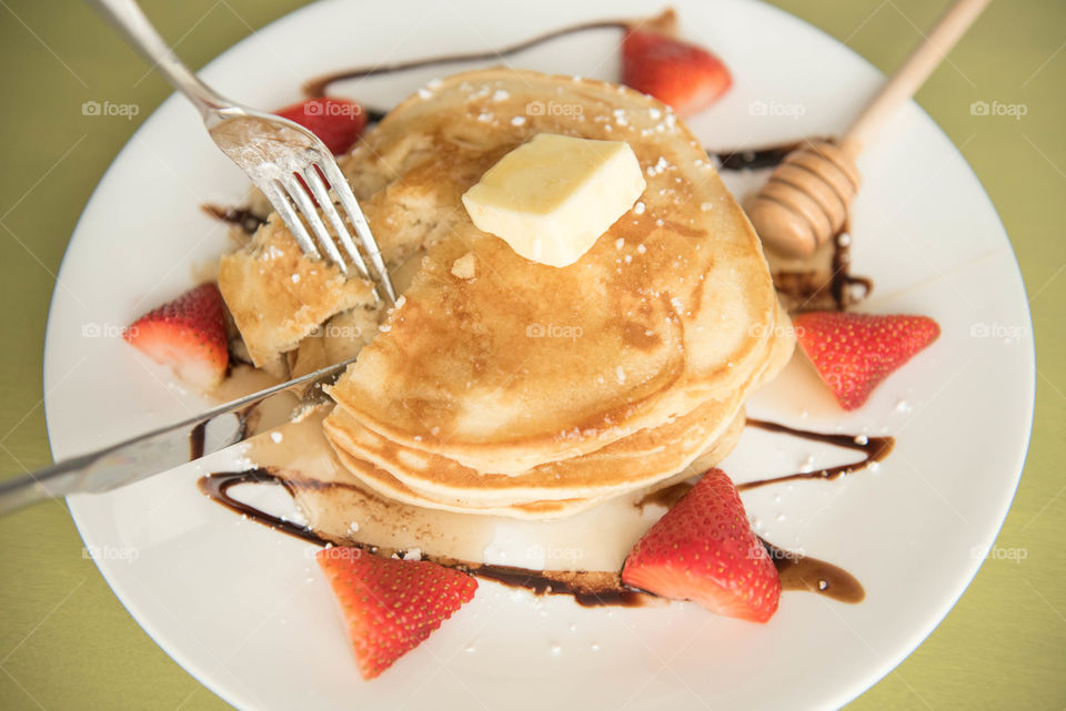 Cutting a stack of pancakes and strawberries with a fork and knife