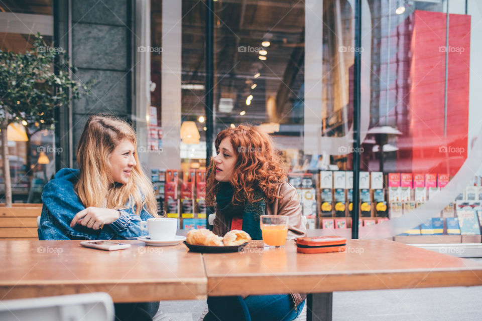 two young women friends sitting at the bar chatting and having breakfast - relaxation, friendship