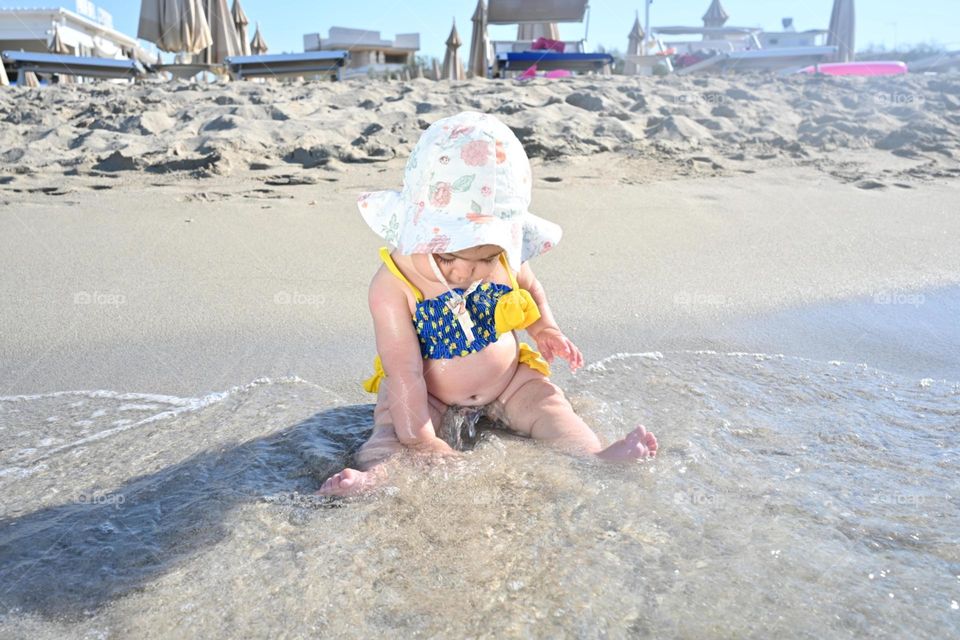 little girl playing by the sea with water and sand