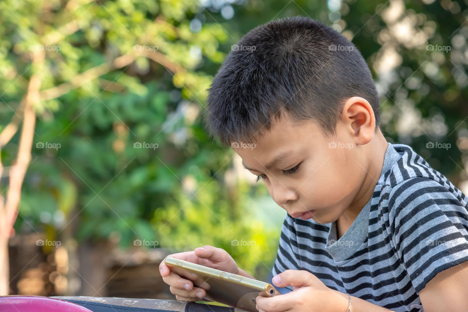 Portrait of Asian boys are playing mobile phones in park.