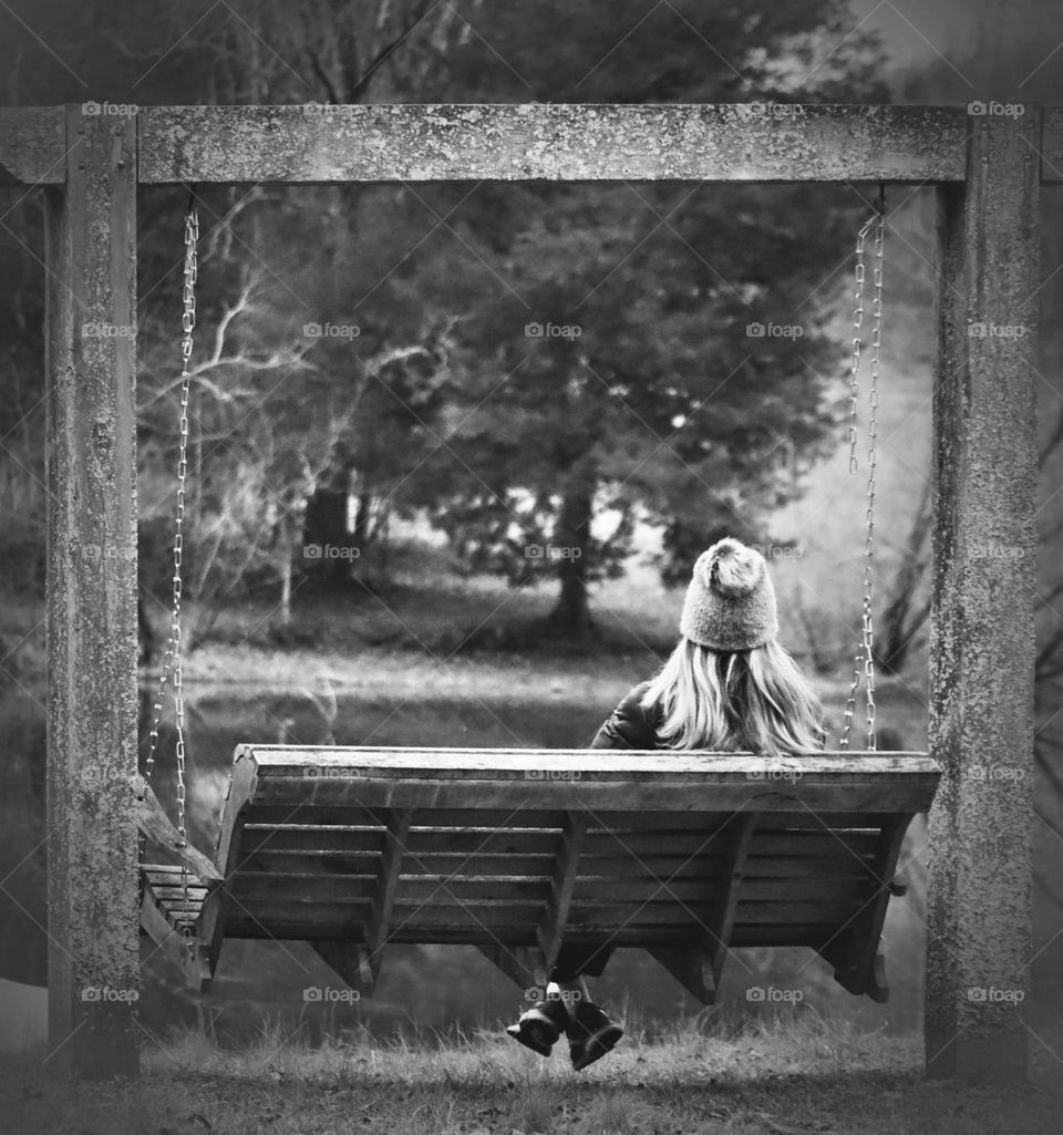 Black and white of athletically dressed woman sitting on a bench swing while looking out onto peaceful pond 