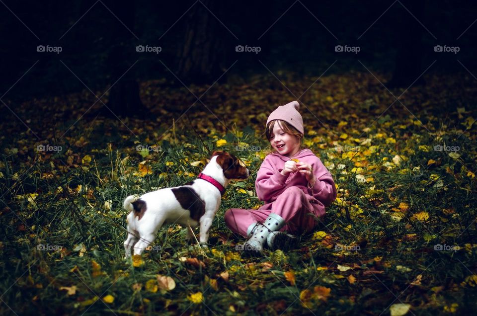 A girl plays with her dog in the autumn forest.