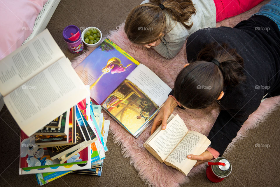 Reading is my ultimate favourite hobby and if I get the opportunity to enjoy it with my little bookworm girl it's my happy place! Image from above with mom and daughter reading together with healthy snacks and stack of books.