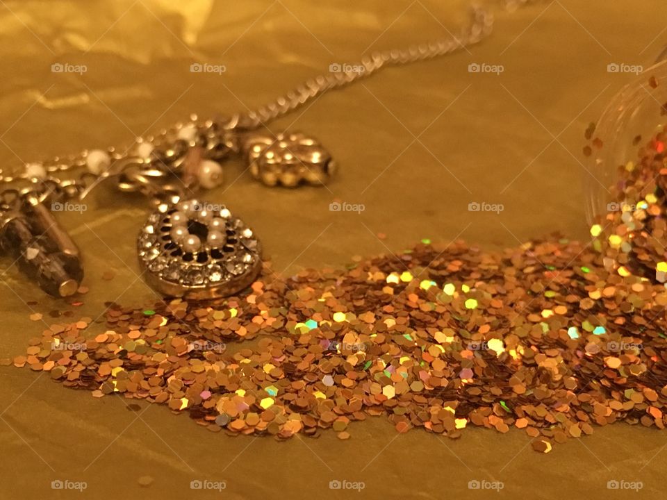Gold charm chain necklace with gold glitter spilled onto gold tissue paper 