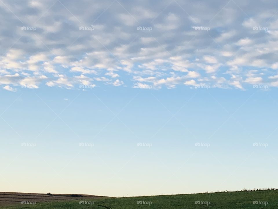 Popcorn clouds above a clear blue sky and empty countryside horizon line