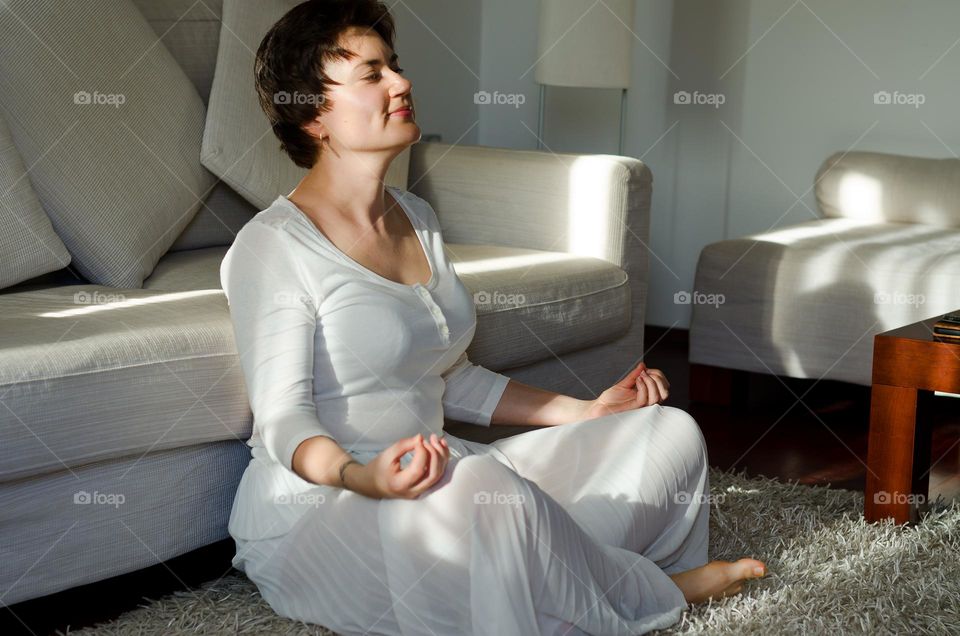 Lifestyle portrait of young, happy, beautiful woman with short hair and no make up. Sitting at cozy home and relaxing. Yoga and meditation.