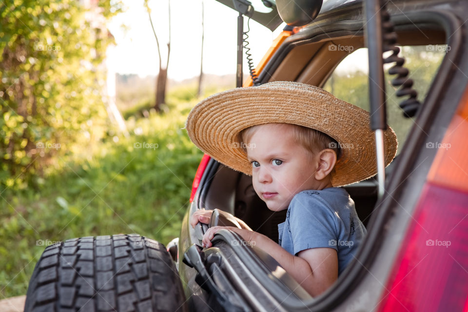 Little toddler boy in hat sitting in car trunk, ready to travel