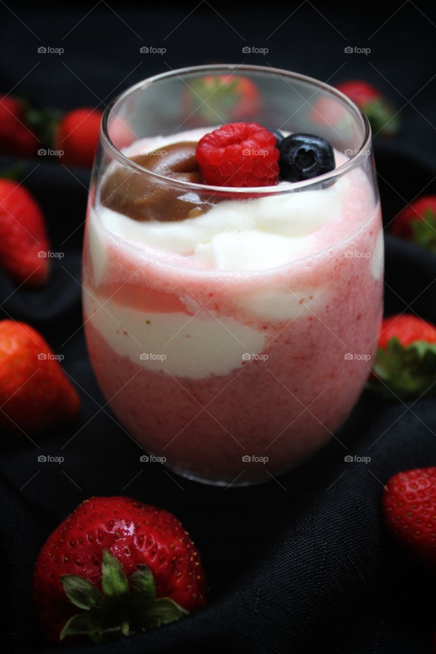 a glass of strawberry milkshake with berries, caramel and vanilla cream on top