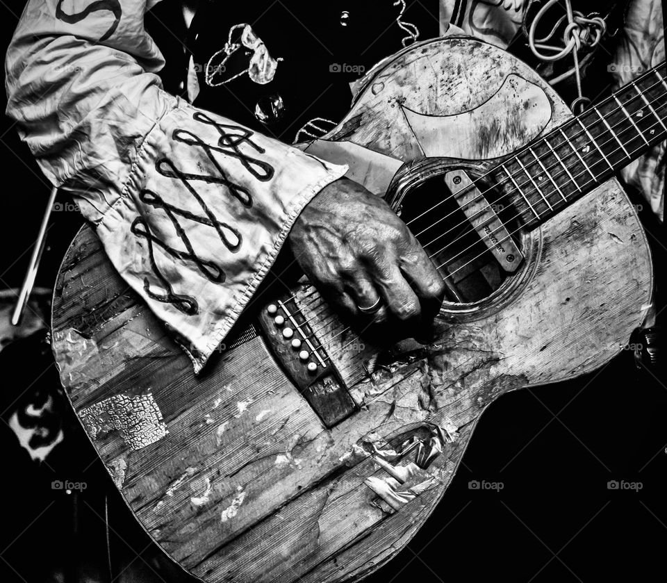 A flamboyantly dressed arm plays a beat up, old acoustic guitar 