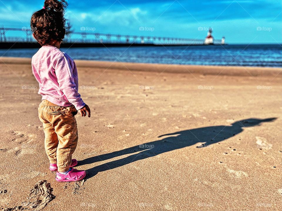 Toddler on the beach looking out to the ocean, moments of happiness on the beach, baby in the beach, standing tall with her shadow on the beach, watching the ocean and lighthouse 