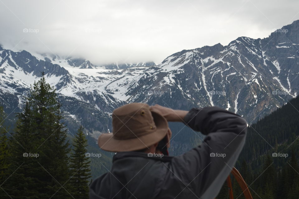 Male photographer in hat in the Rocky Mountains capturing a photo of mountains with camera 