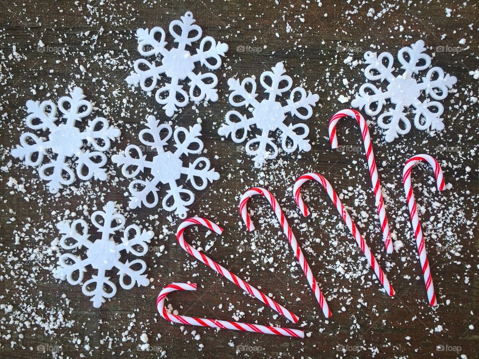 Candy canes on rustic wooden table powdered with snow and snowflakes 