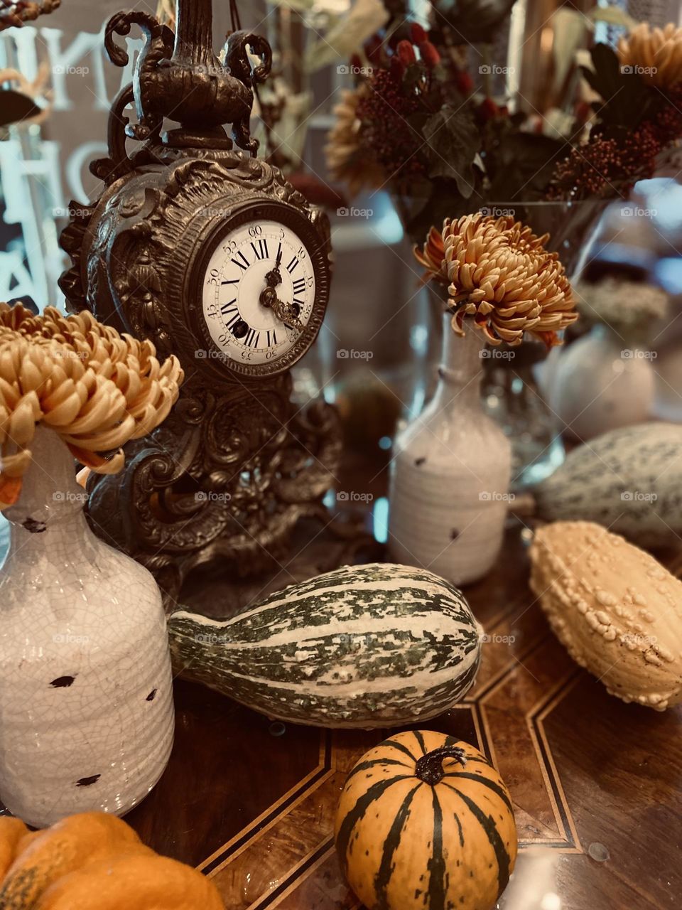 A vintage clock on a a table with various squash and pumpkins representing the Autumn season.
