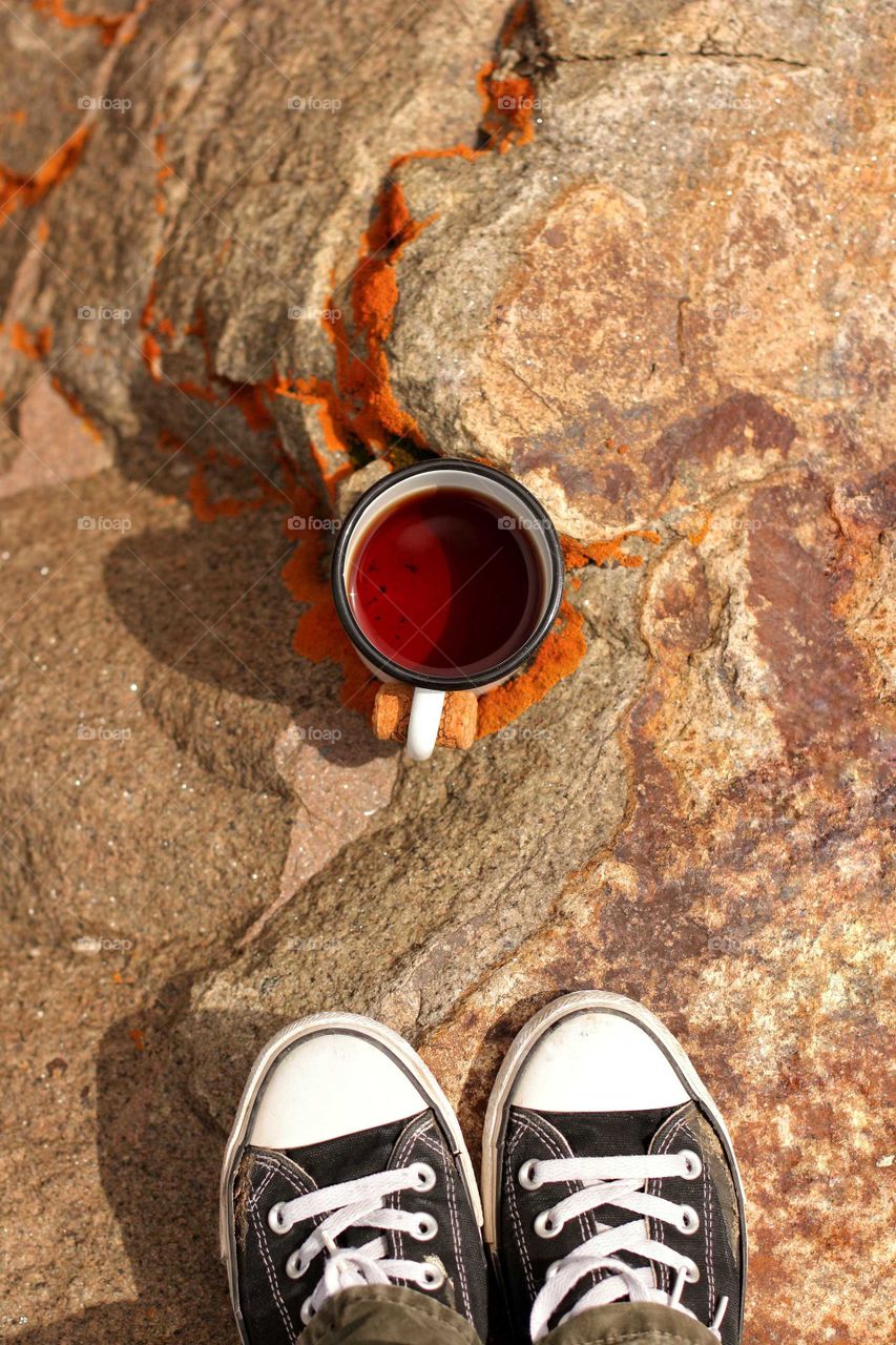 Self portrait in sneakers, on a rock with mosses and lichens with a cup of hot tea in the mountains in the trip