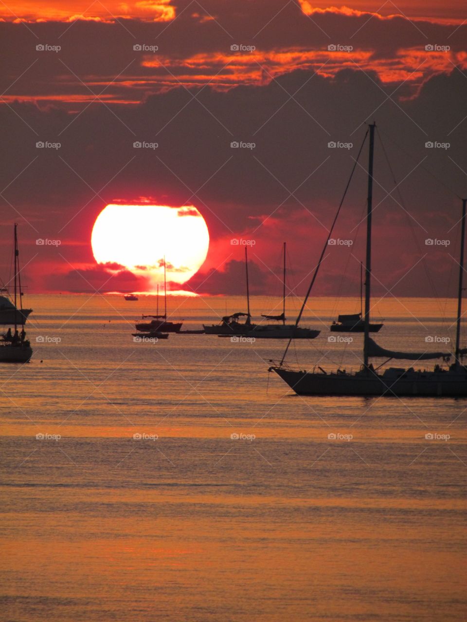 Large sun setting over water colorful sky and reflecting on the water. Boats at anchor. 