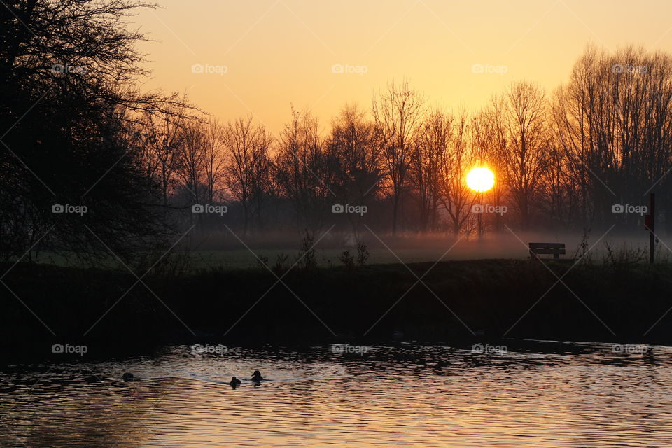 Amazing colourful sunset with an eerie cold fog along the riverbank ...