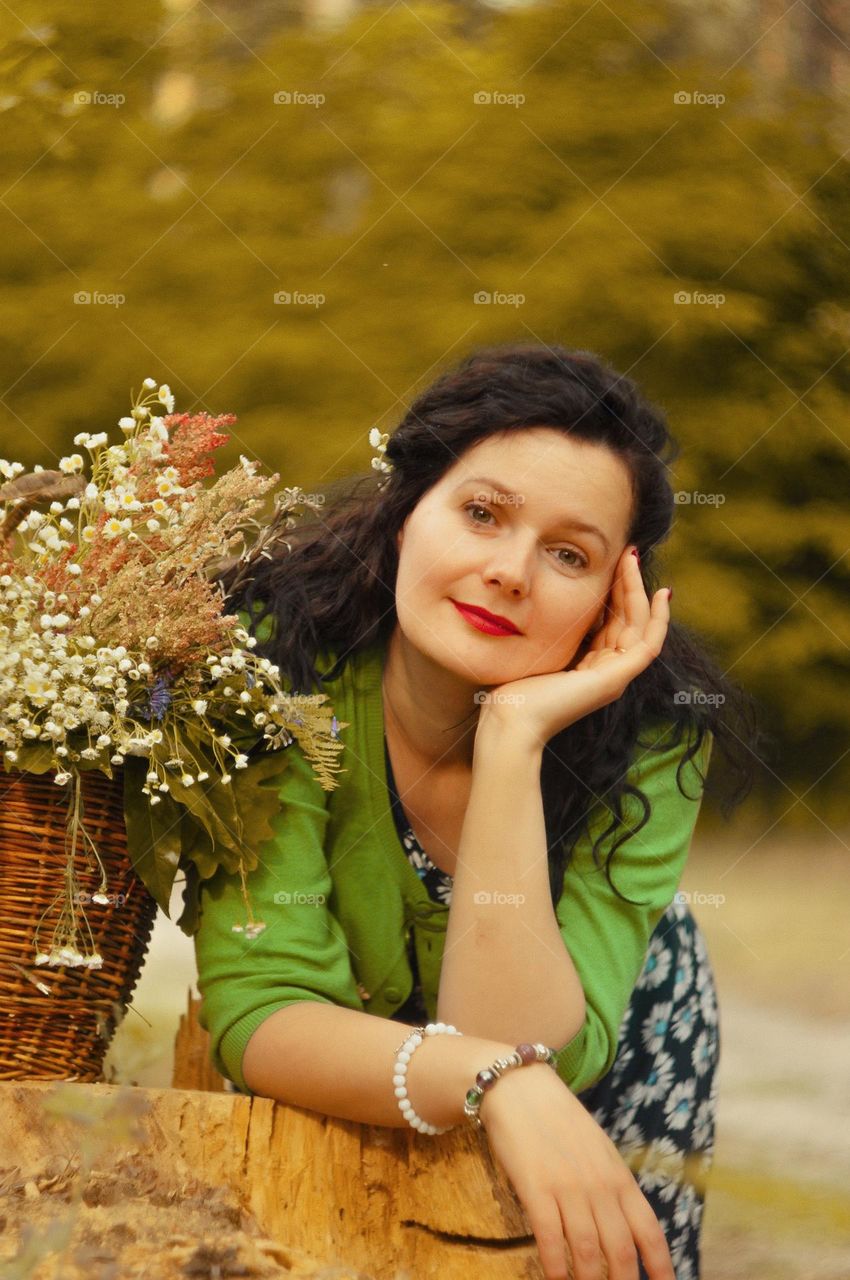 portrait of a mother in a green forest with a basket of flowers