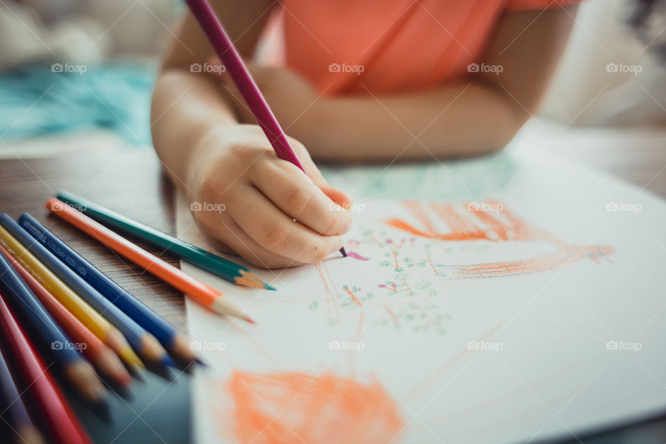 Little girl drawing with colorful pencils at wooden desk indoor