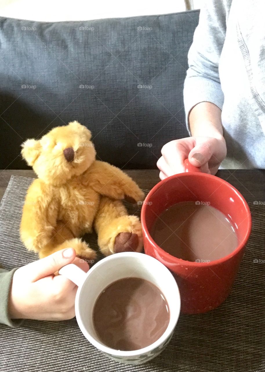 A young child and his mother holding a cup of hot chocolate at the dinner table with their friends bear. Mother and son sharing a cup of hot chocolate. USA, America