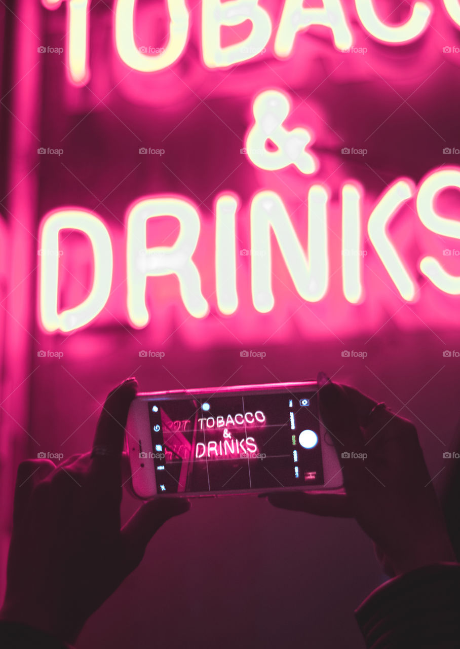 Girl holding a phone towards a neon sign.