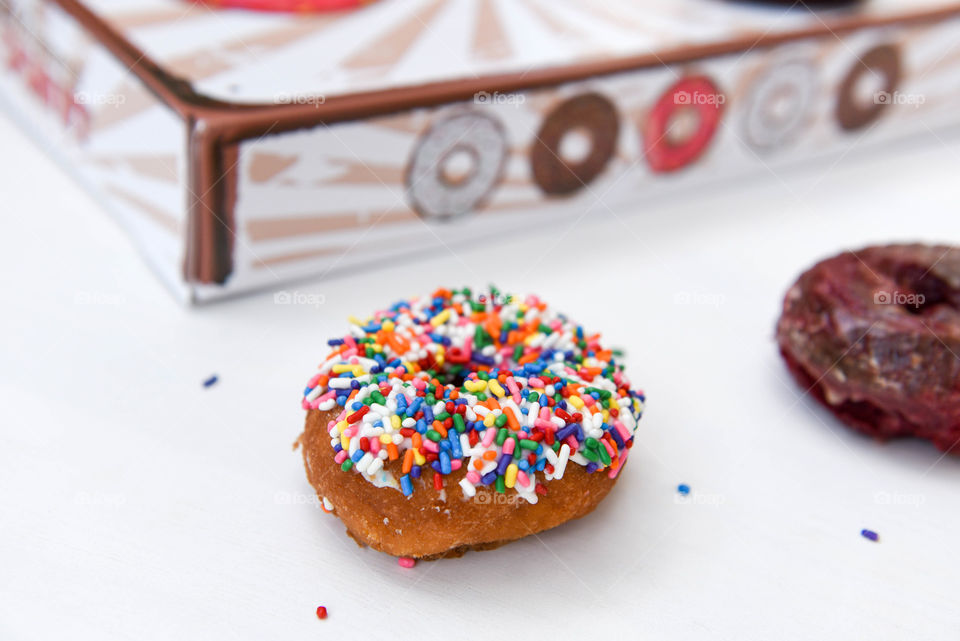 Rainbow sprinkles donut on a table next to a donut box
