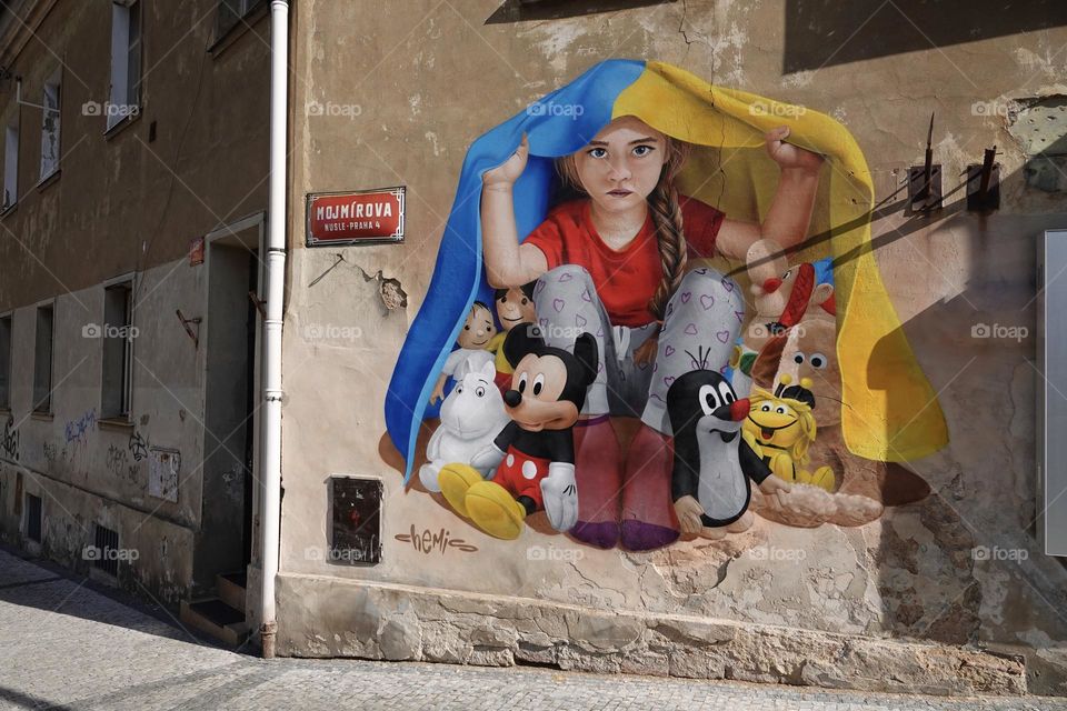 Mural of girl with toys hidding under Ukrainian flag by Czech street atrist of Kazakh origin Chemis in Mojmirova street in Prague 4 Nusle. Support to Ukraine in war against Russia.