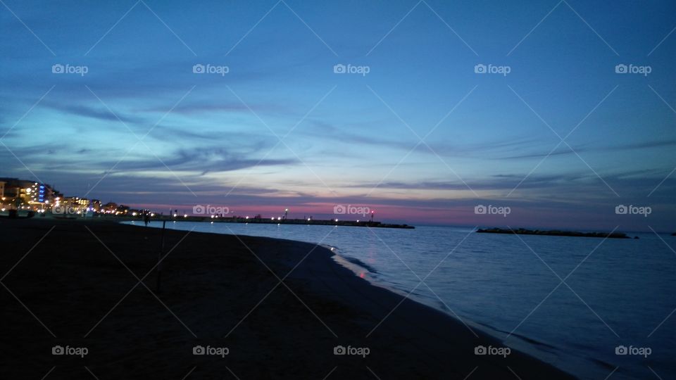 Italy coast sea beach sunset colored pink and blue sky with city lights