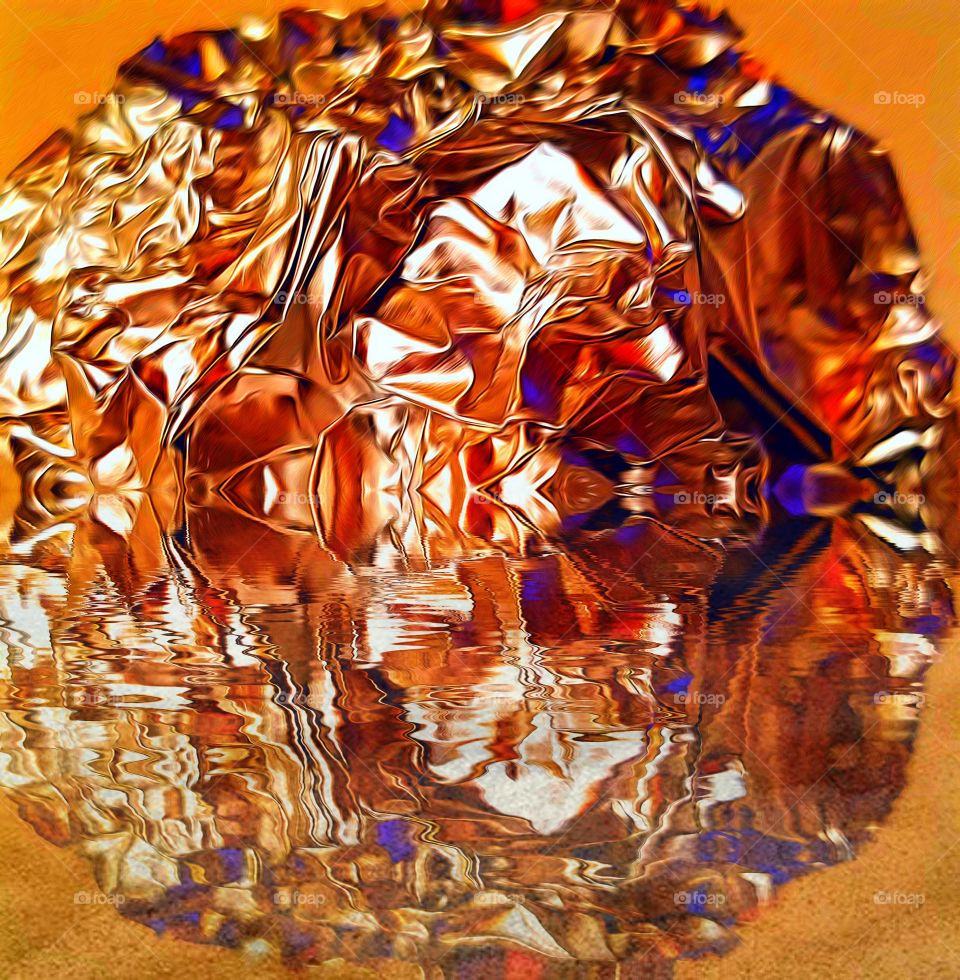 Crumpled ball of foil under orange light, reflected in water.