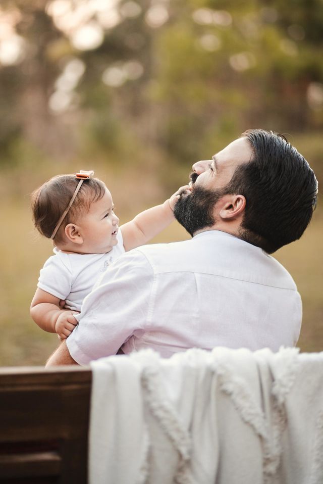 Loving father playing with daughter, making her giggle as they sit on a bench at the park.