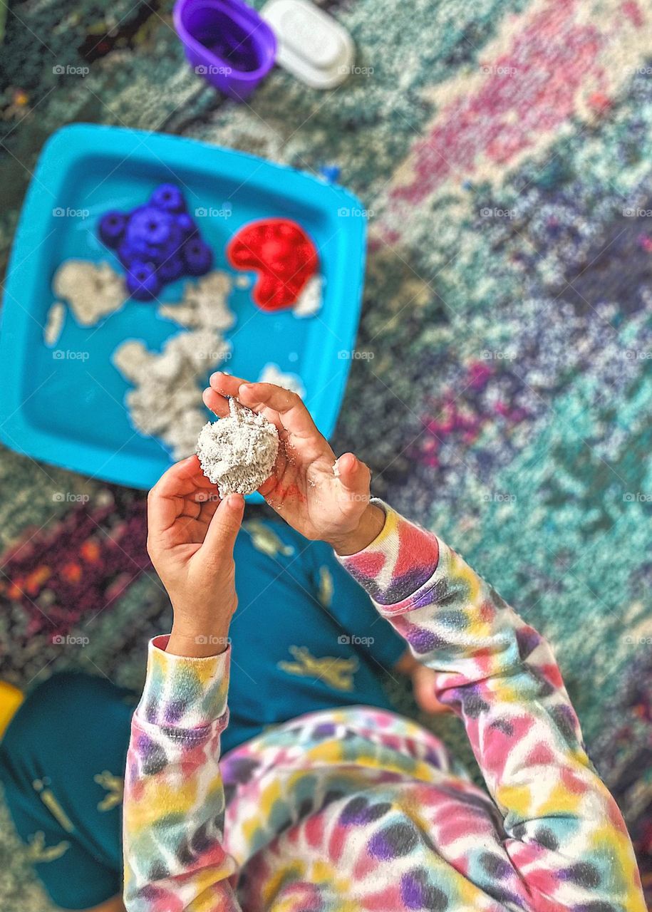 Toddler girl plays with white Kinetic Sand, toddler creates sculpture out of sand indoors, wintertime creative activities with children, creating with kids indoors, fun activities with toddlers, Kinetic Sand art with toddlers, aerial view of playing