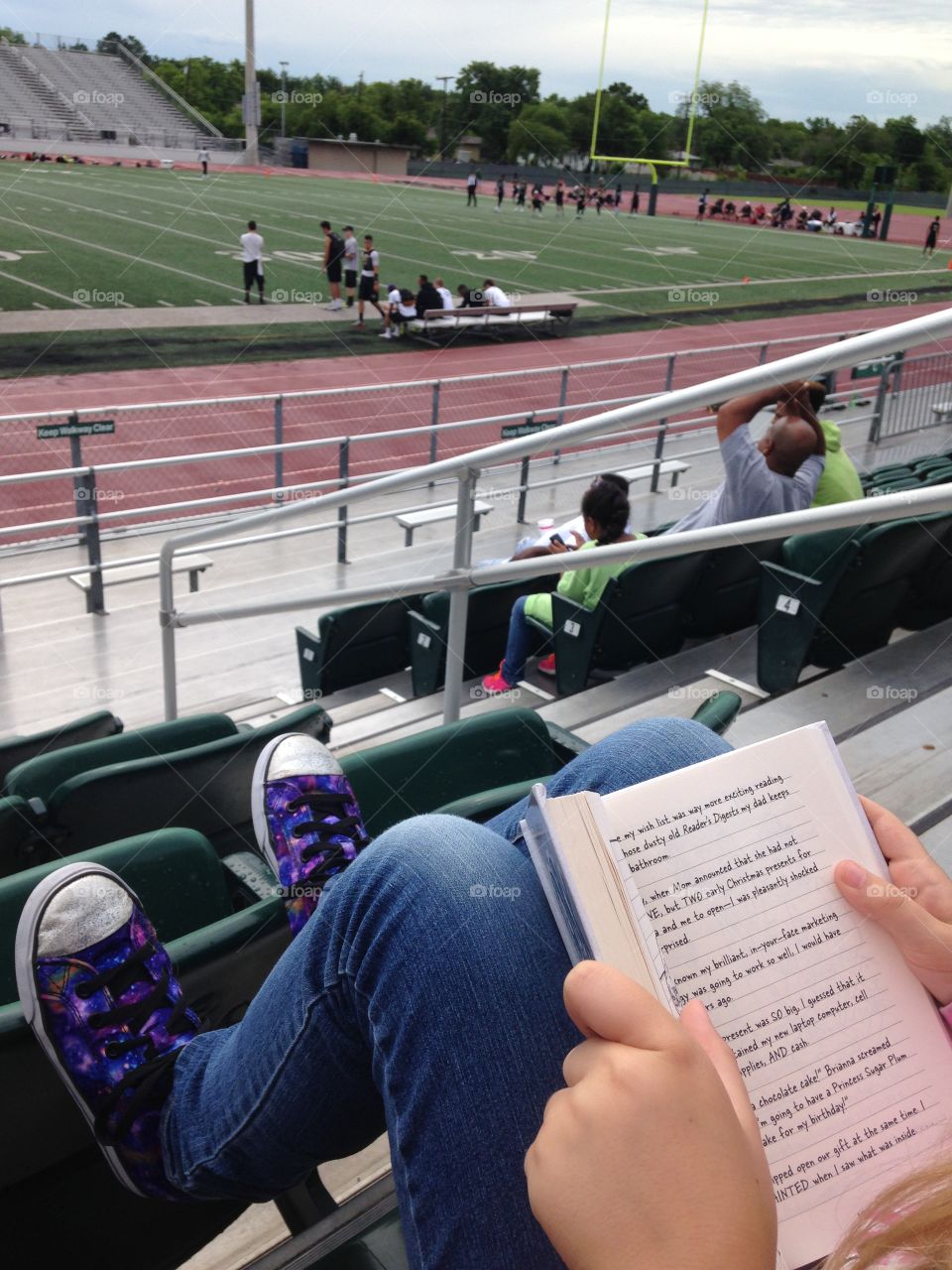 Football and reading. A girl reading a book and watching 7 on 7 football