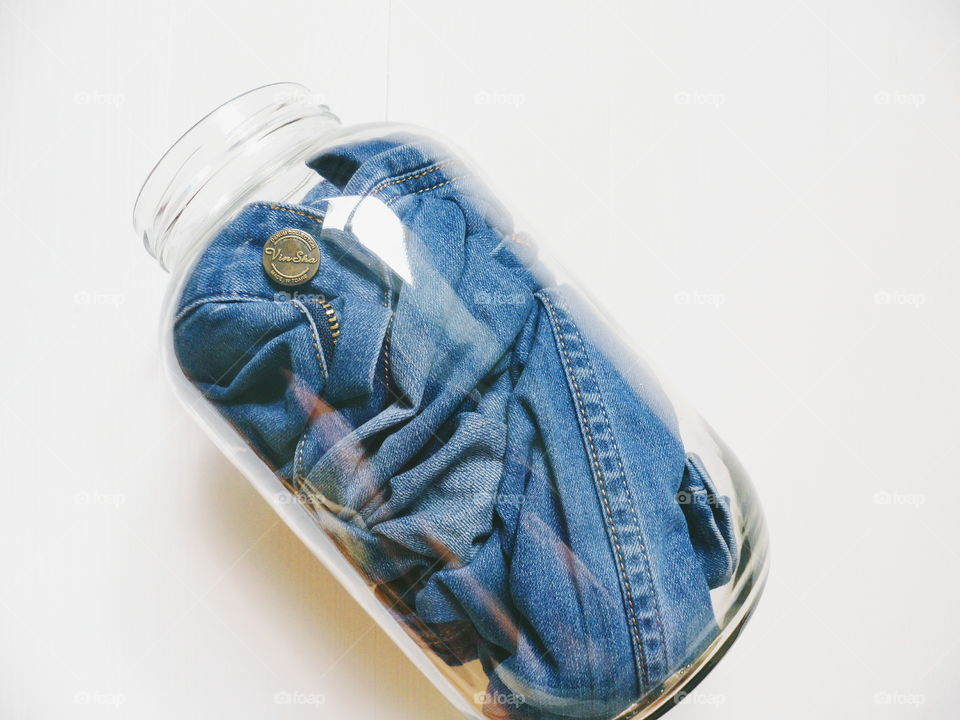 in a glass jar men's jeans pants on a white background