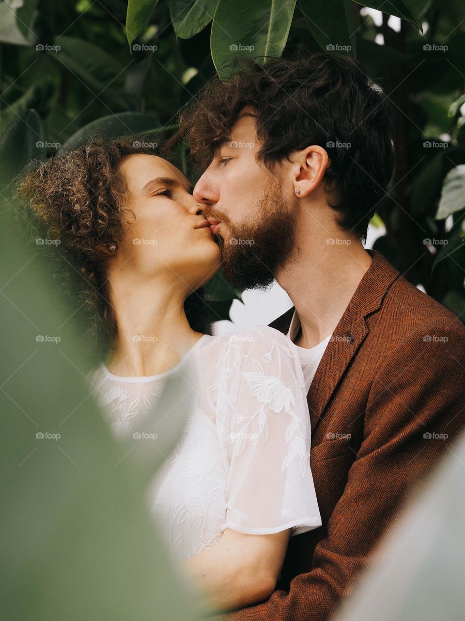 Young beautiful lovers kissing in botanical garden 