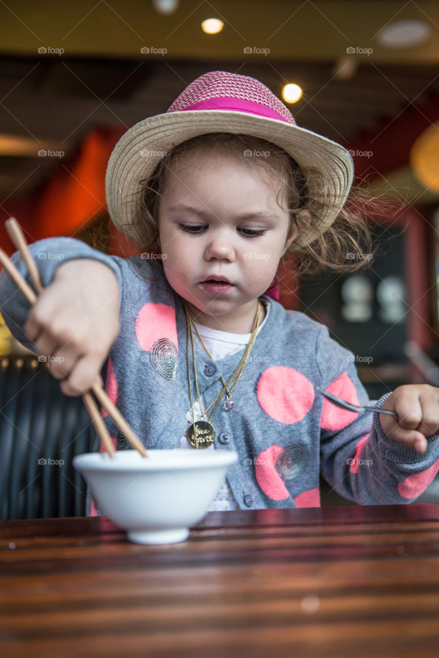 Little girl holding chopstick and eating food