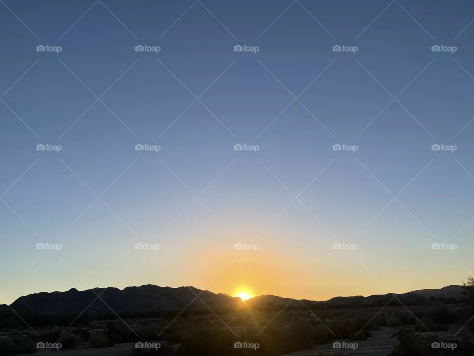 A orange and yellow sunset with the sun above the mountains.