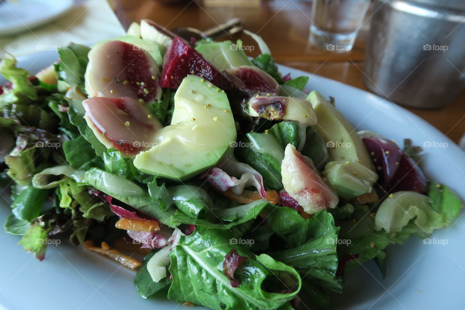 Green salad with Greek Mykonean pig cold cuts called Louza, served on a white plate with green vegetables, avocado and fig.