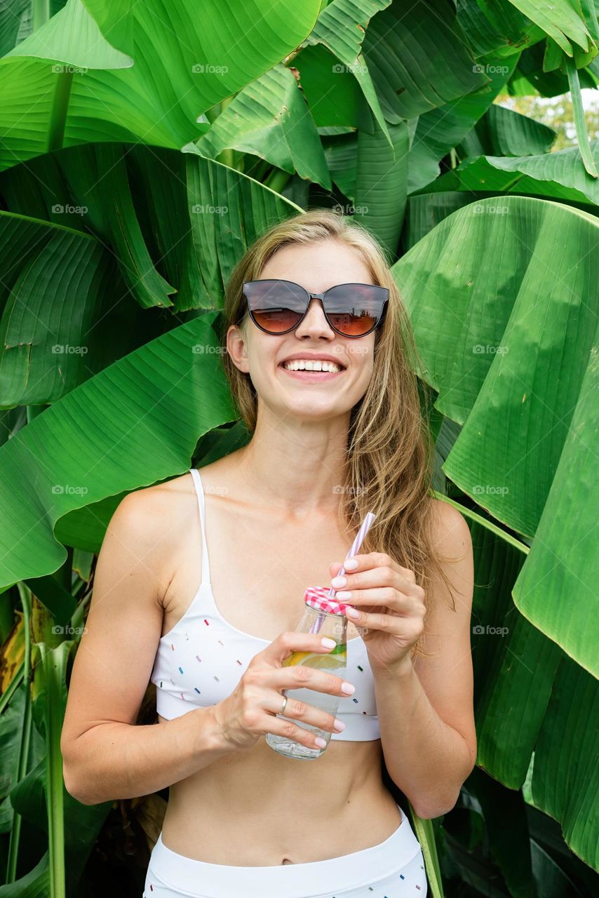 smiling woman in palm tree in swim suit drink