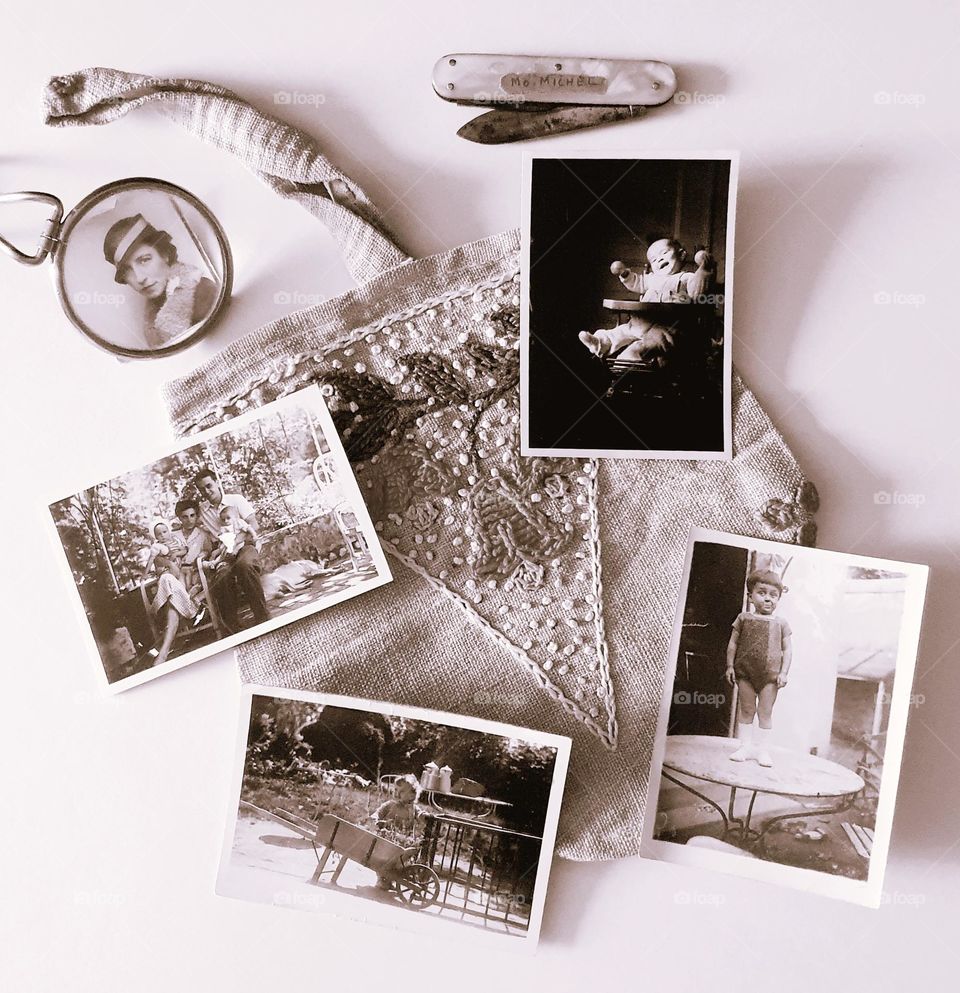 Sepia shot of a vintage flatlay placed on a cream surface and composed of handmade handbag, a mother-of-pearl penknife, a pocket magnifying glass and 5 vintage photos