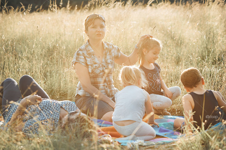 Family spending time together on a meadow, close to nature. Parents and children sitting and playing on a blanket on grass. Candid people, real moments, authentic situations