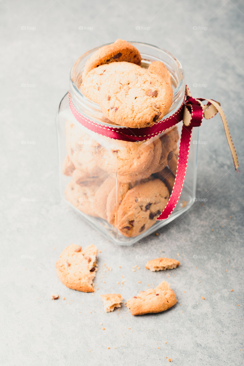 Big jar filled with oat cookies standing on a table. Plain background. Portrait orientation