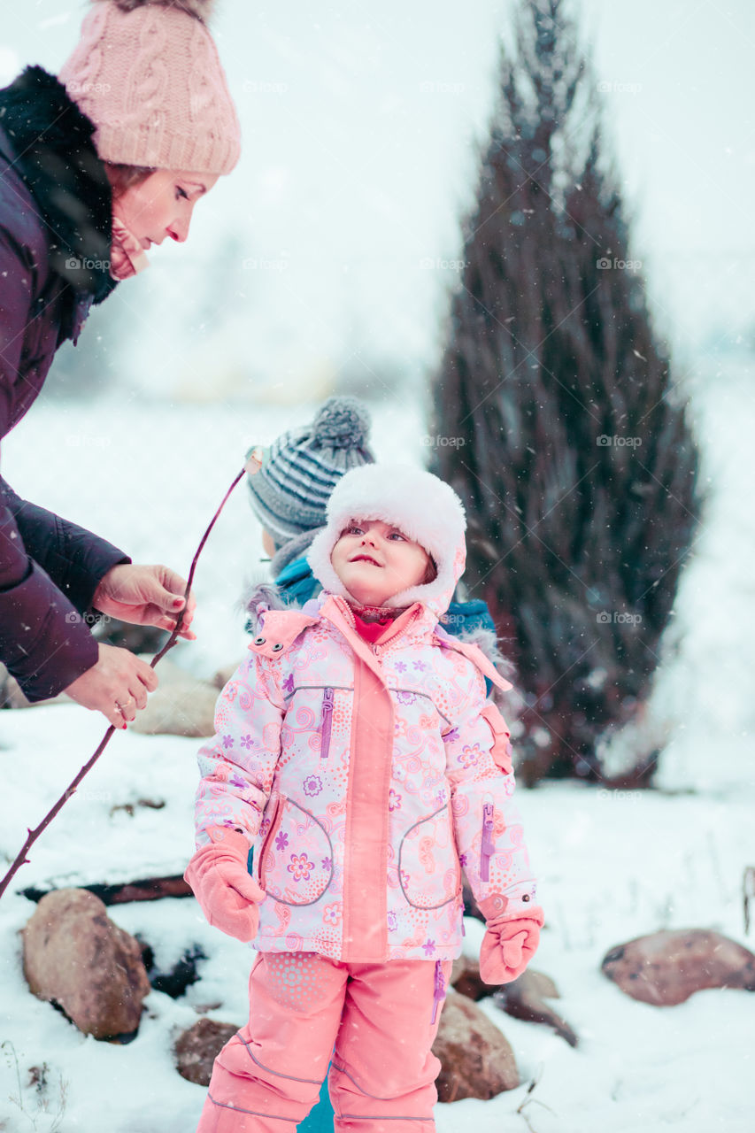 Mom and her little daughter preparing marshmallows on stick to toasting over campfire outdoors in the winter. Woman and girl wearing warm clothes