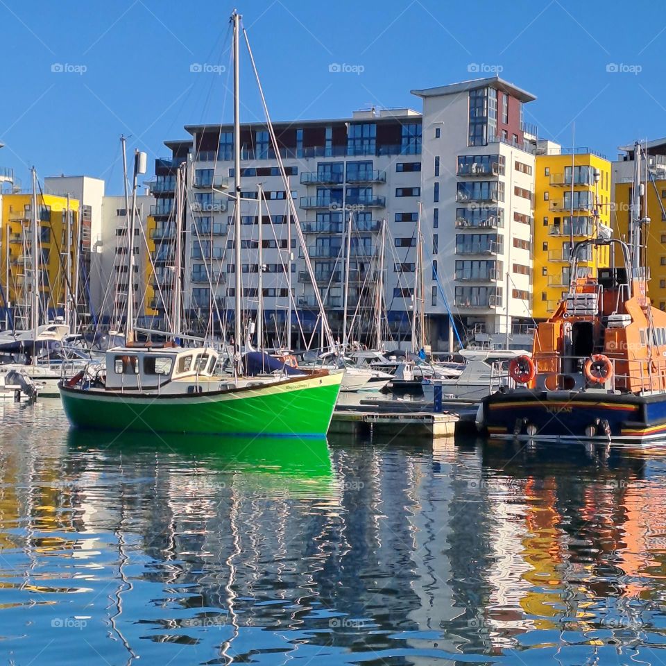 brigjt green and orange boats moored up near yellow and white buildings. reflections on water. bright October day. u.k