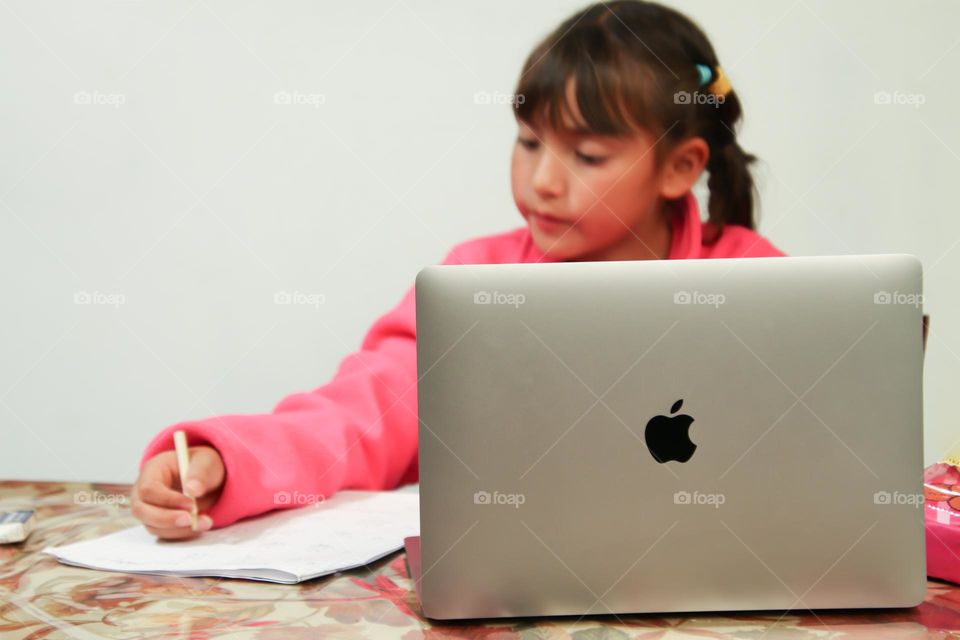 Cute girl is doing her homework with the use of a MacBook