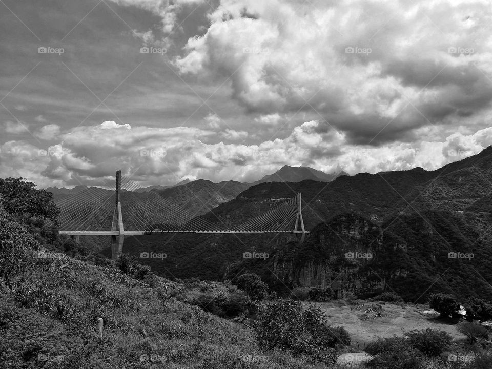 Long bridge crossing between two mountains and a storm coming in the sky, in monochrome style.